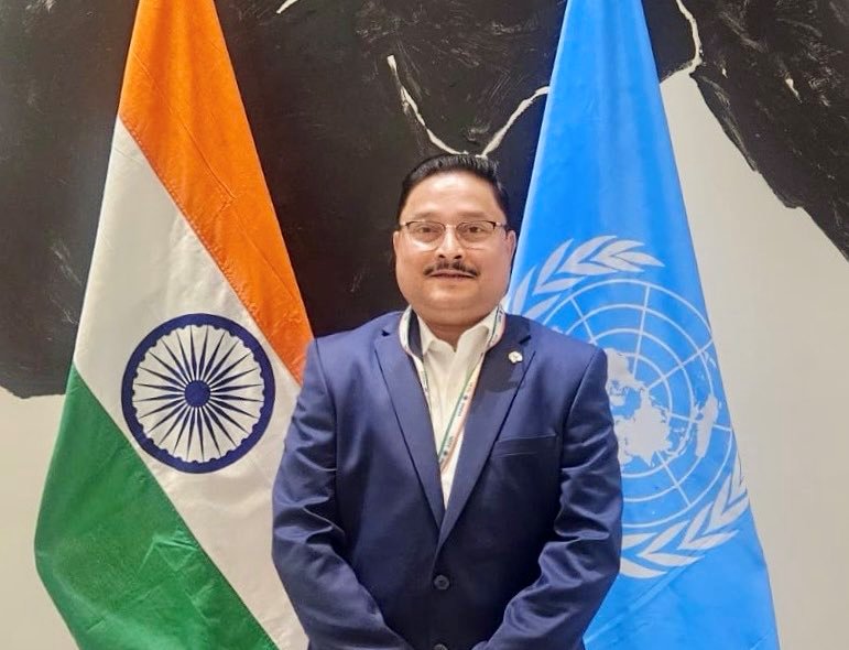 Indian MP Dilip Saikia standing in front of an Indian and UN flags