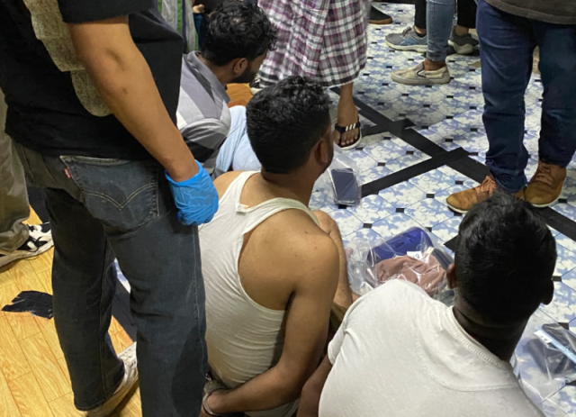 Suspected drug offenders — all migrant workers in Singapore — are handcuffed and questioned by Singapore law enforcement officers while their dorm room is searched