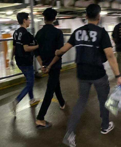 An arrested migrant worker is led away by CNB Singapore officers